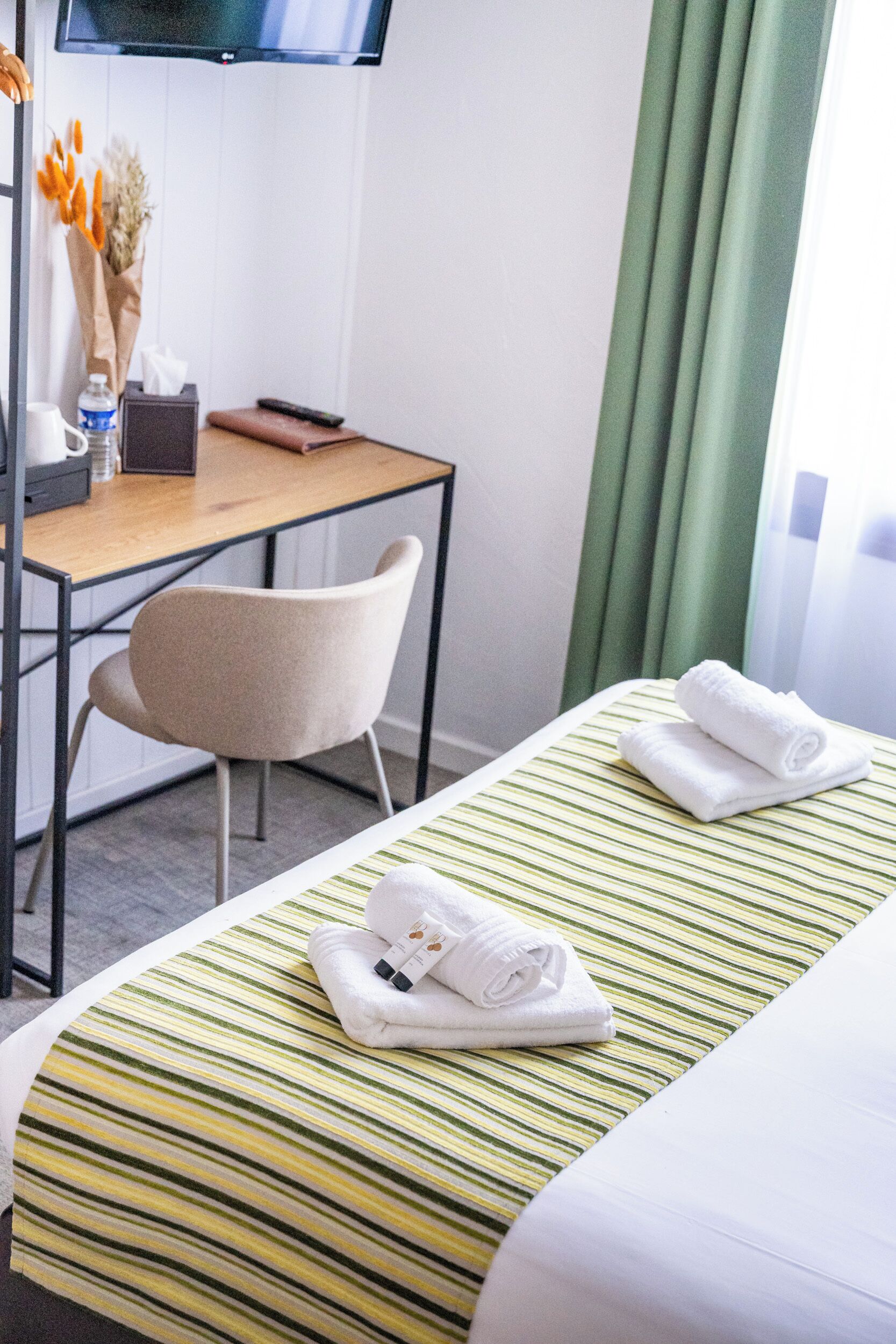 Ein Hotelzimmer mit Bett, Schreibtisch, Stuhl, Fernseher und einem Fenster mit Vorhängen.