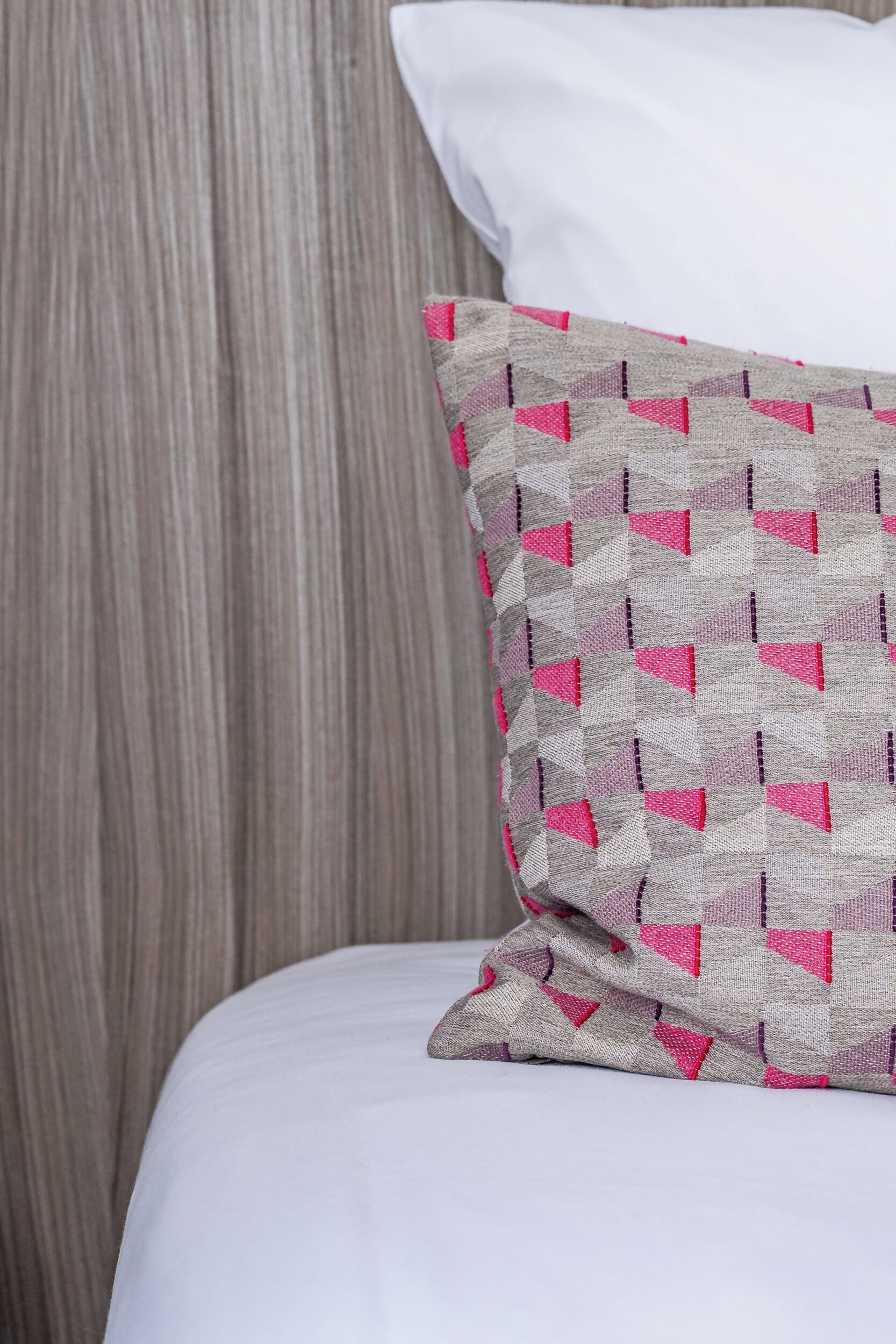 A bed with a white sheet and a pillow with a geometric pattern.