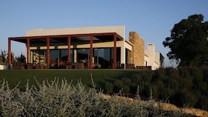 A modern house with a large glass facade, a stone exterior, and a well-maintained lawn. - Quinta do Mel (Albufeira)