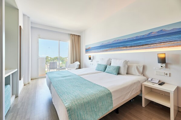 Habitación de hotel con una cama grande, un escritorio, una silla, un cuadro de playa y vistas al exterior.