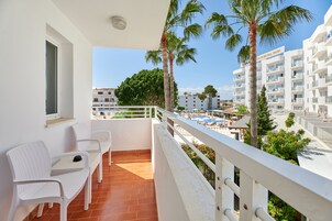 Un balcón con sillas blancas, piscina y palmeras.