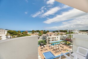 Zona de piscina en la azotea con sillones de descanso y sombrillas, con vista a una playa y al paisaje urbano.