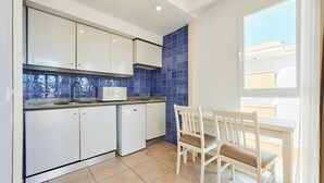 A kitchen with white cabinets, a microwave, and a blue tiled backsplash. There is a window with a view of buildings outside. - Aluasun Continental Park Hotel & Apartments (Muro)