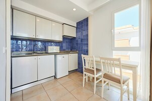 Una cocina con armarios blancos, un microondas y un salpicadero de azulejos azules. Se ve una ventana con vistas a edificios.