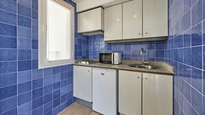 A compact kitchen with blue tiles, a microwave, a sink, and white cabinets. - Aluasun Continental Park Hotel & Apartments (Muro)