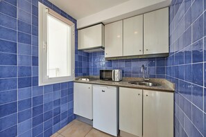 Cocina compacta con azulejos azules, un microondas, un lavamanos y armarios blancos.