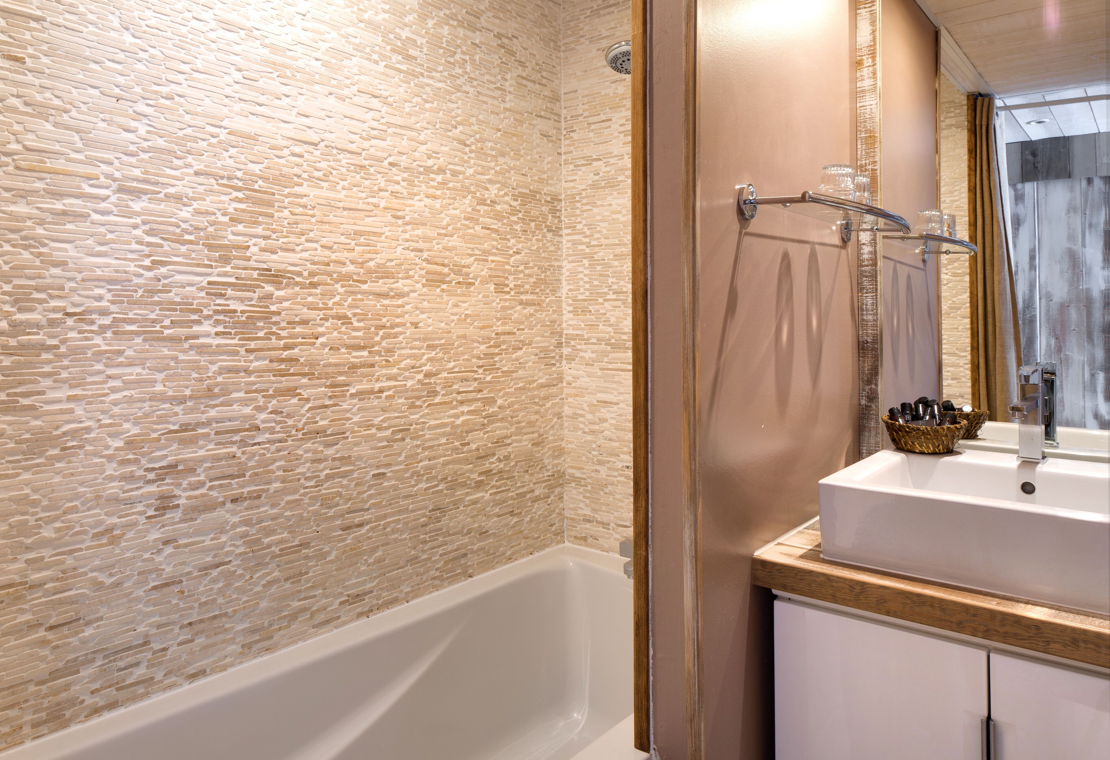 Ein Badezimmer mit einer Wand mit Steinoptik, einer weißen Badewanne, einem Waschbecken mit Spiegel und einem Handtuchhalter.