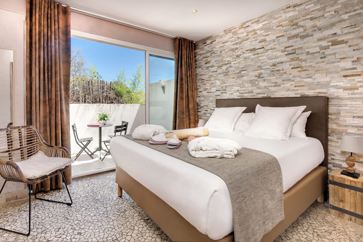 A hotel room with a large bed, a small table, a chair, and a view of the outdoors.
