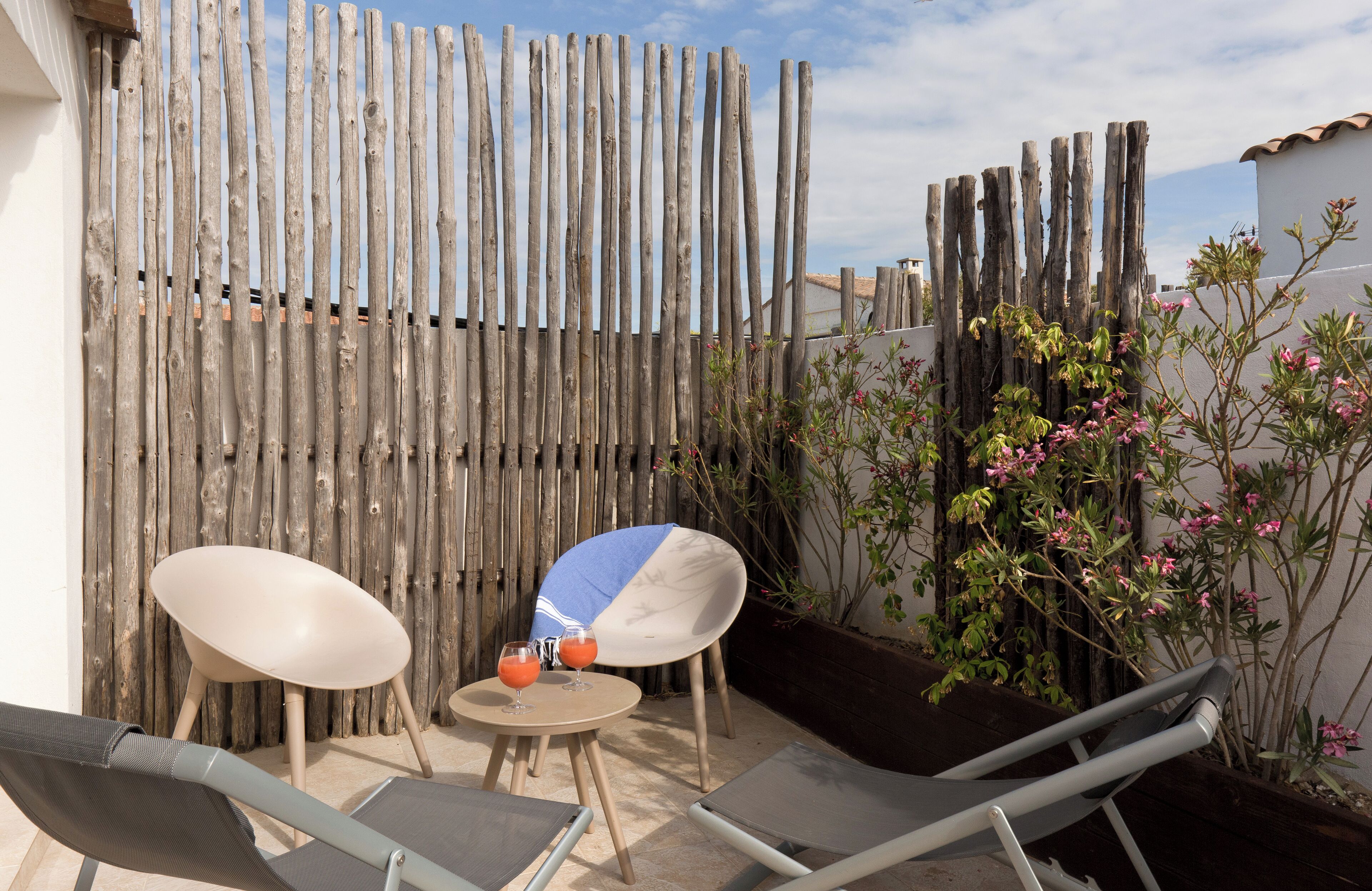 A patio with two lounge chairs, a small round table, and a drink.