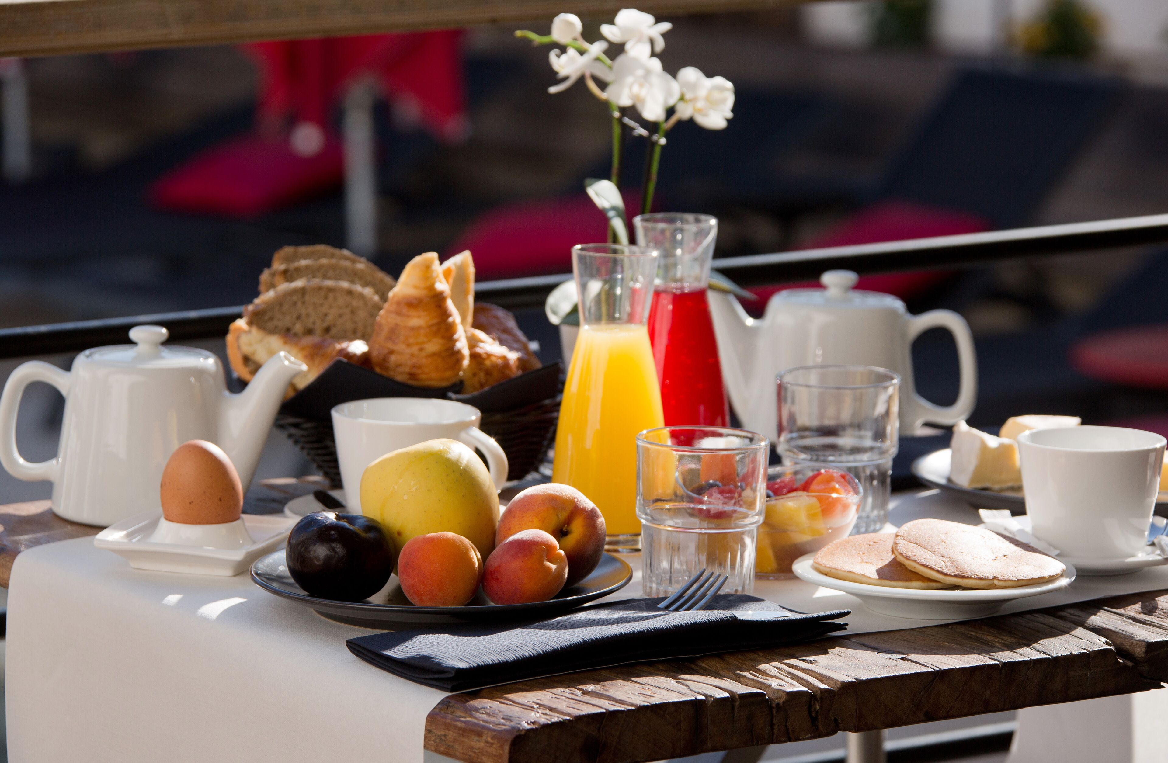 Una mesa de desayuno con tetera, tazas, jarra y diversas frutas y pasteles.