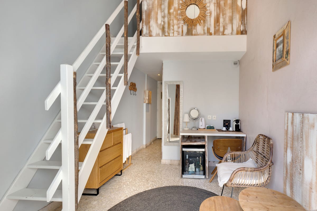A modern interior with a staircase, a wooden dresser, a desk with a mirror, and a wicker chair.
