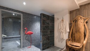 A bathroom with a glass shower enclosure, a red flamingo decoration, a wooden chair, and a wooden wall panel. - Vila de la Mar & Spa (Saintes-Maries-de-la-Mer)