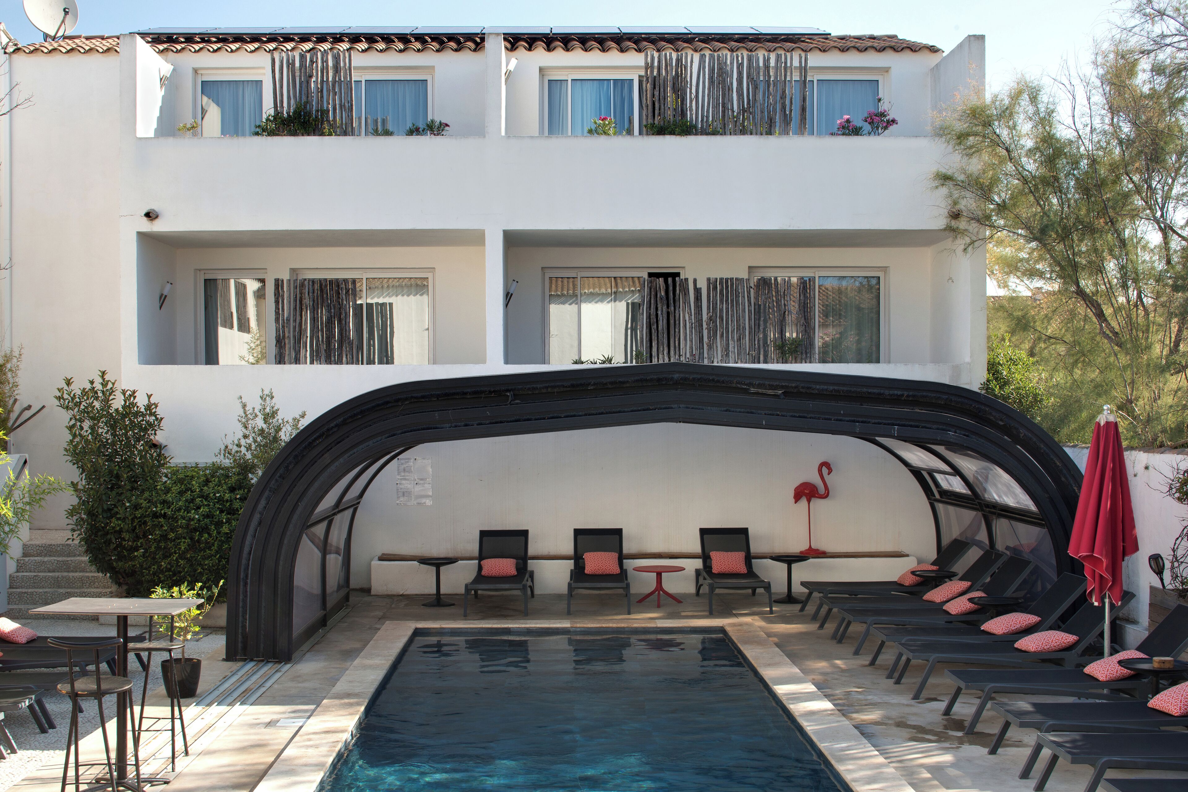 Un edificio de dos pisos con piscina, sillas de descanso y una zona de estar cubierta.