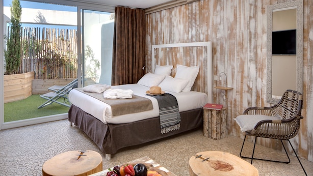 A hotel room with a bed, a dining table with fruit, a wicker chair, and a view of the outdoors. - Vila de la Mar & Spa (Saintes-Maries-de-la-Mer)