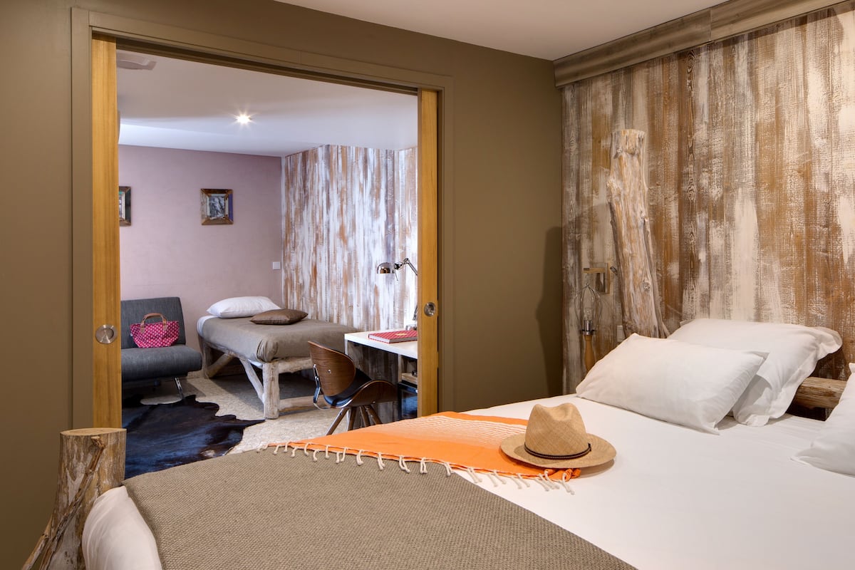 A hotel room with a bed, a desk, a chair, and a door leading to another room.