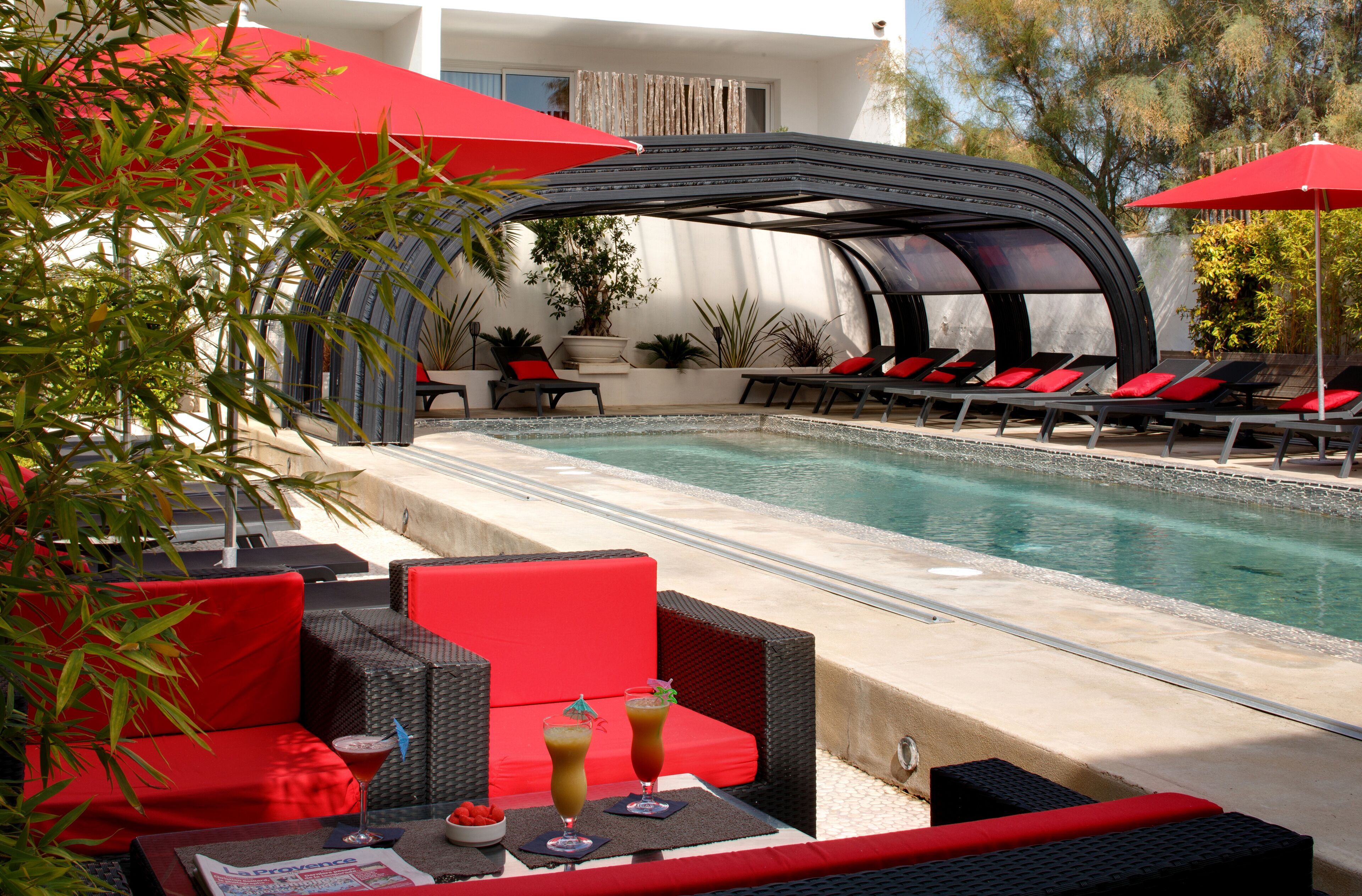 Un espace aménagé au bord de la piscine, avec des chaises longues, un coin salon abrité et une table avec des boissons.