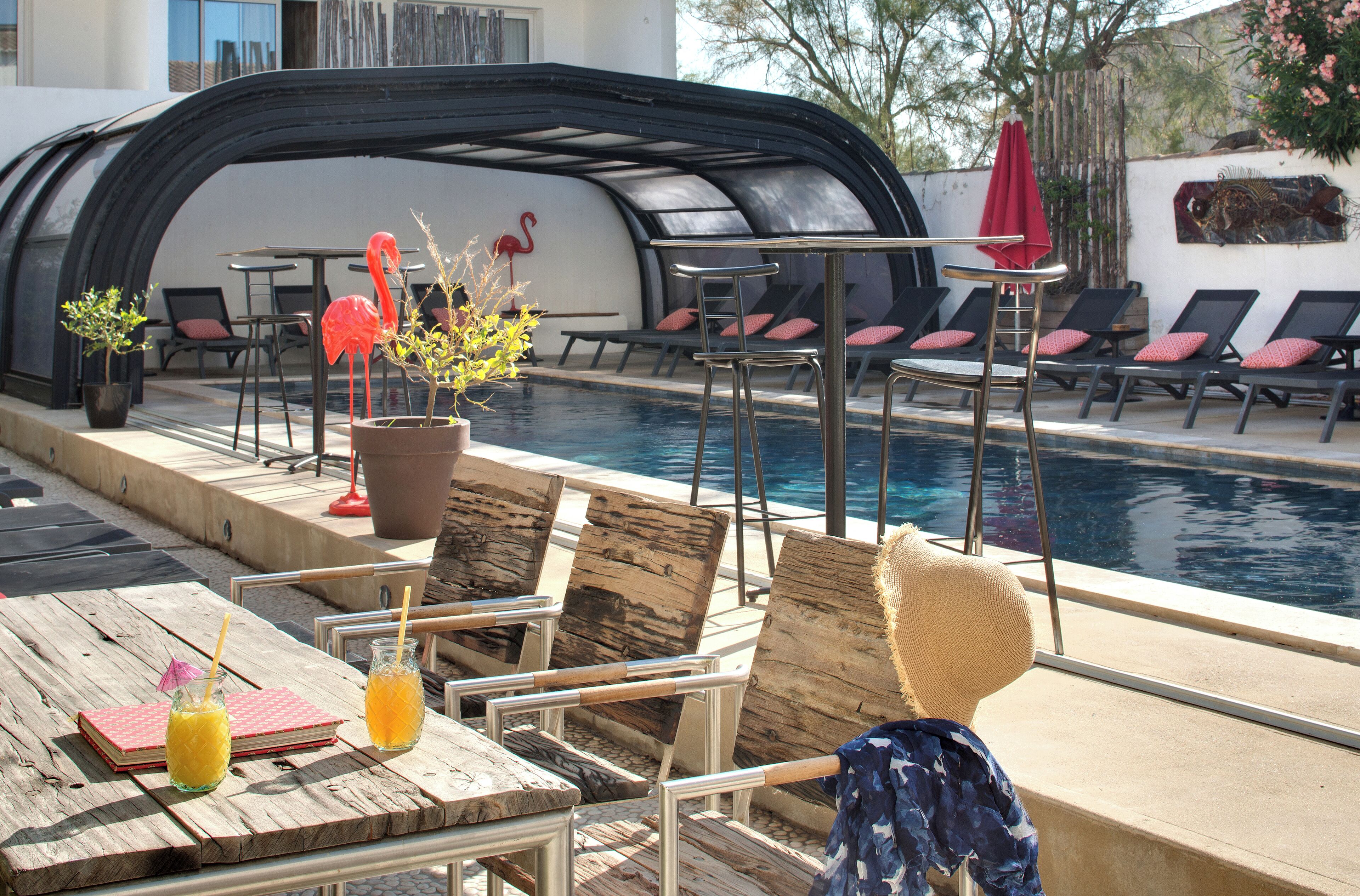 Un espace aménagé au bord de la piscine, avec des chaises longues, une table où sont servis des boissons et un coin salon abrité.