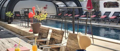 Un espace aménagé au bord de la piscine, avec des chaises longues, une table où sont servis des boissons et un coin salon abrité.