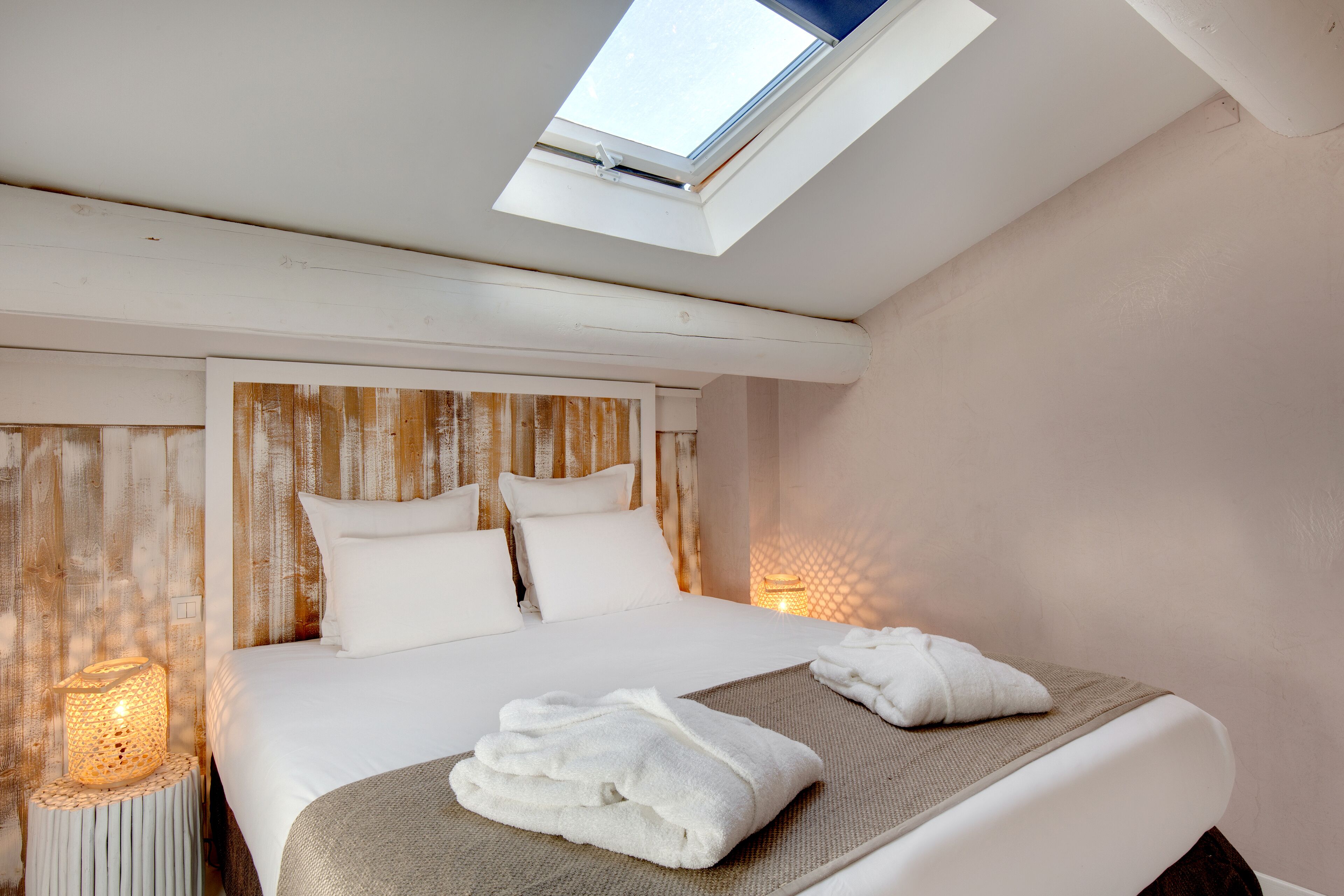 Una habitación de hotel con tragaluz, una cama con sábanas blancas y una lámpara de noche.