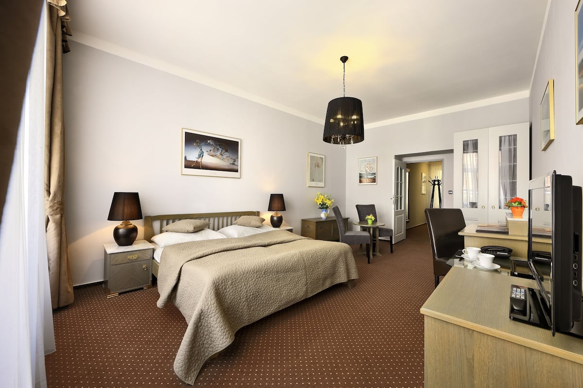 Een hotelkamer met een bed, nachtkastjes, een bureau met stoel, een televisie en een zithoek met een tafel en stoelen.