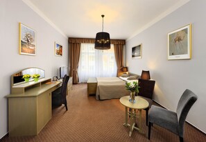 A hotel room with a bed, desk, chair, and a small table with flowers. - Hotel Salvator (Prague)