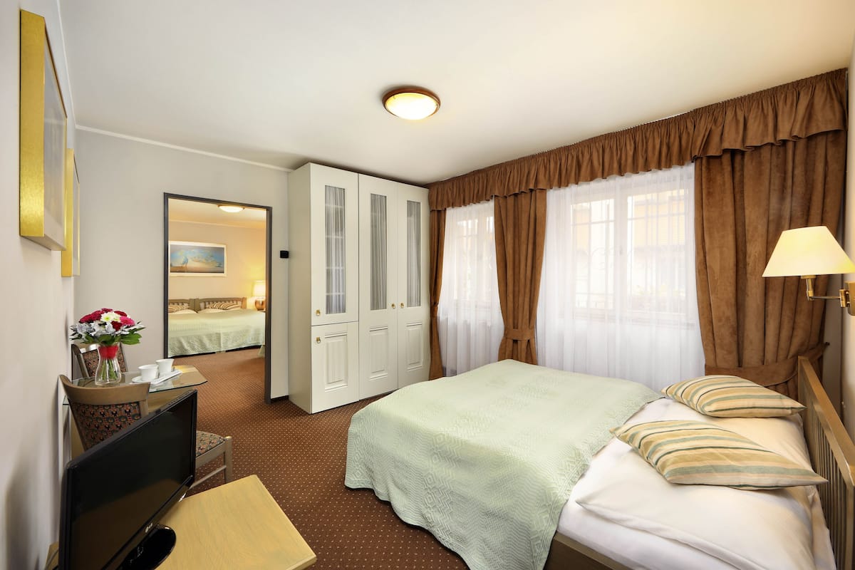 Een hotelkamer met een bed, een bureau met een computer, een stoel, een televisie, een lamp en een raam met gordijnen.