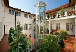 A courtyard with a glass elevator, potted plants, and a tiled floor. - Hotel Salvator (Prague)