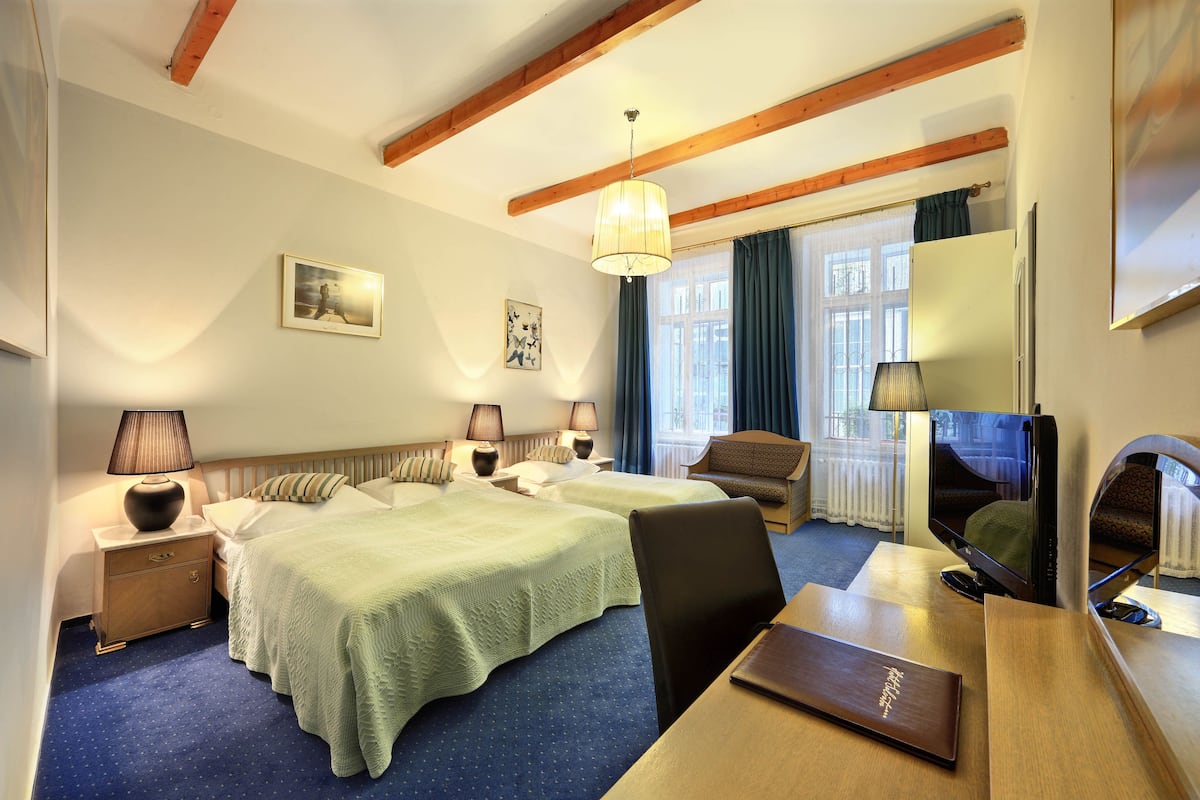 Een hotelkamer met twee bedden, een bureau, een stoel, een televisie en een raam met gordijnen.