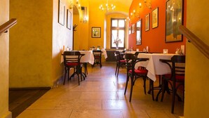 A restaurant with tables and chairs, a staircase, and framed artwork on the walls. - Hotel Rous (Plzen)