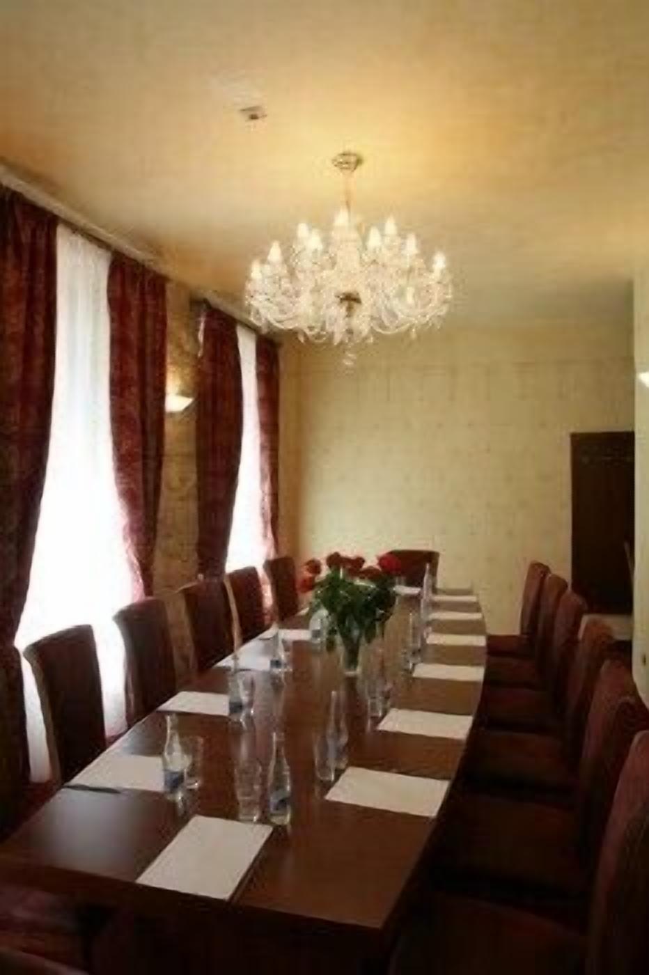 Un salón de conferencias con una larga mesa, sillas, una araña y un jarrón con flores.