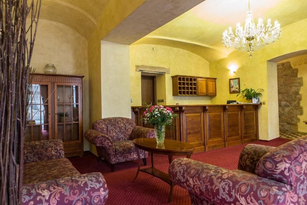 A room with patterned sofas, a wooden cabinet, a chandelier, and a red carpet.