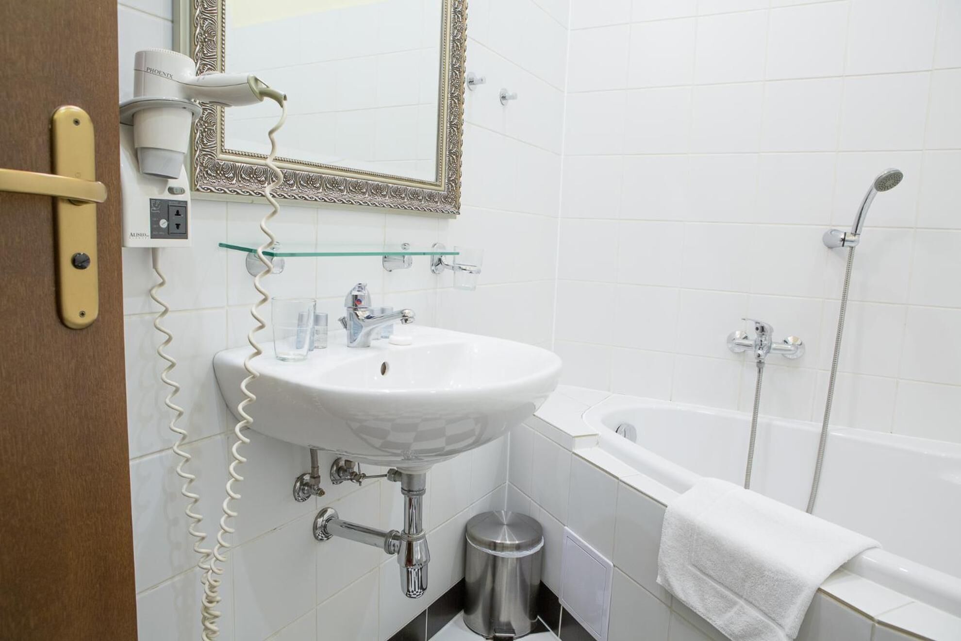 Een badkamer met een wit wastafel, een spiegel, een haardroger, een douche en een handdoek aan de muur.