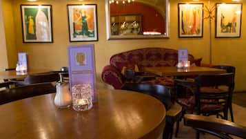 Interior de restaurante con mesas redondas, sillas y obras de arte enmarcadas en las paredes.