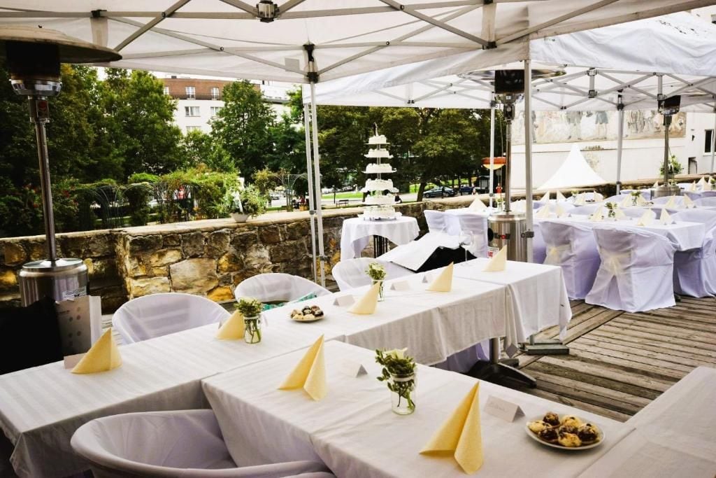 An outdoor dining area with tables set for a wedding reception, featuring a tiered wedding cake centerpiece.
