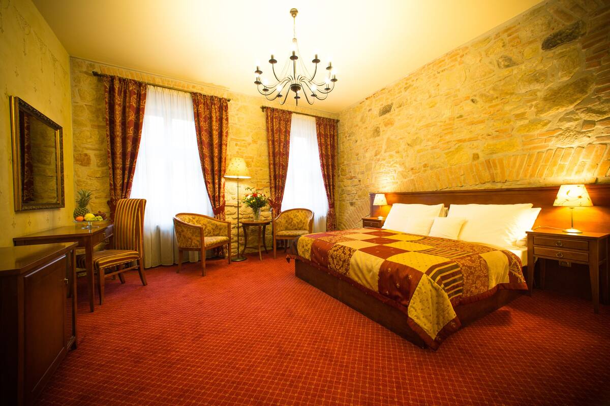 Una habitación de hotel con una cama grande, un escritorio con silla, una mesita de noche con lámpara y un candelabro.