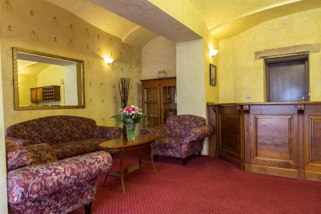 A room with patterned sofas, a wooden table with a vase of flowers, a mirror, and a wooden cabinet.