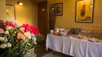 A dining area with a table set for a meal, a floral arrangement in the foreground, and artwork on the walls.
