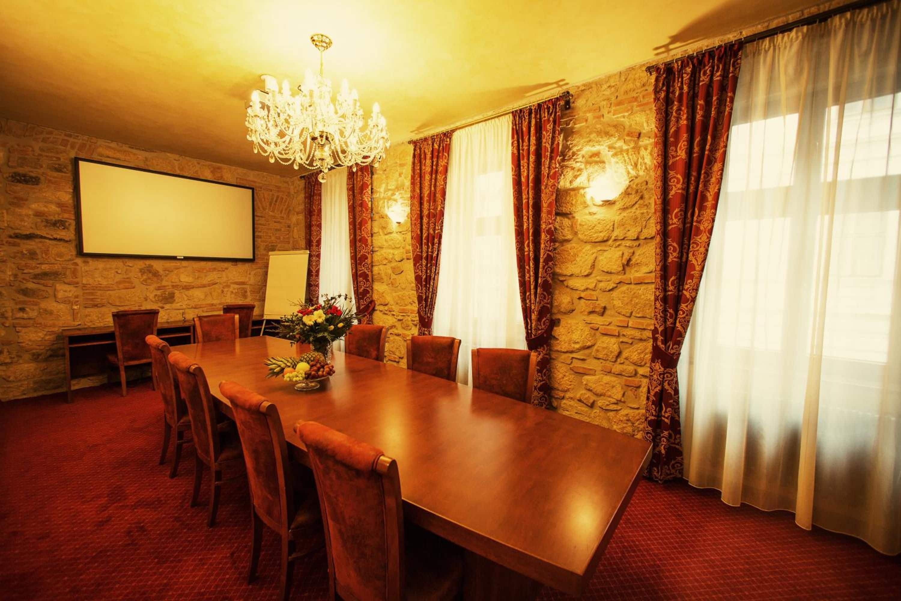 Ein Konferenzraum mit einem langen Tisch, Stühlen, einer Projektionsleinwand, einer Kristallleuchtre und Steinwänden.
