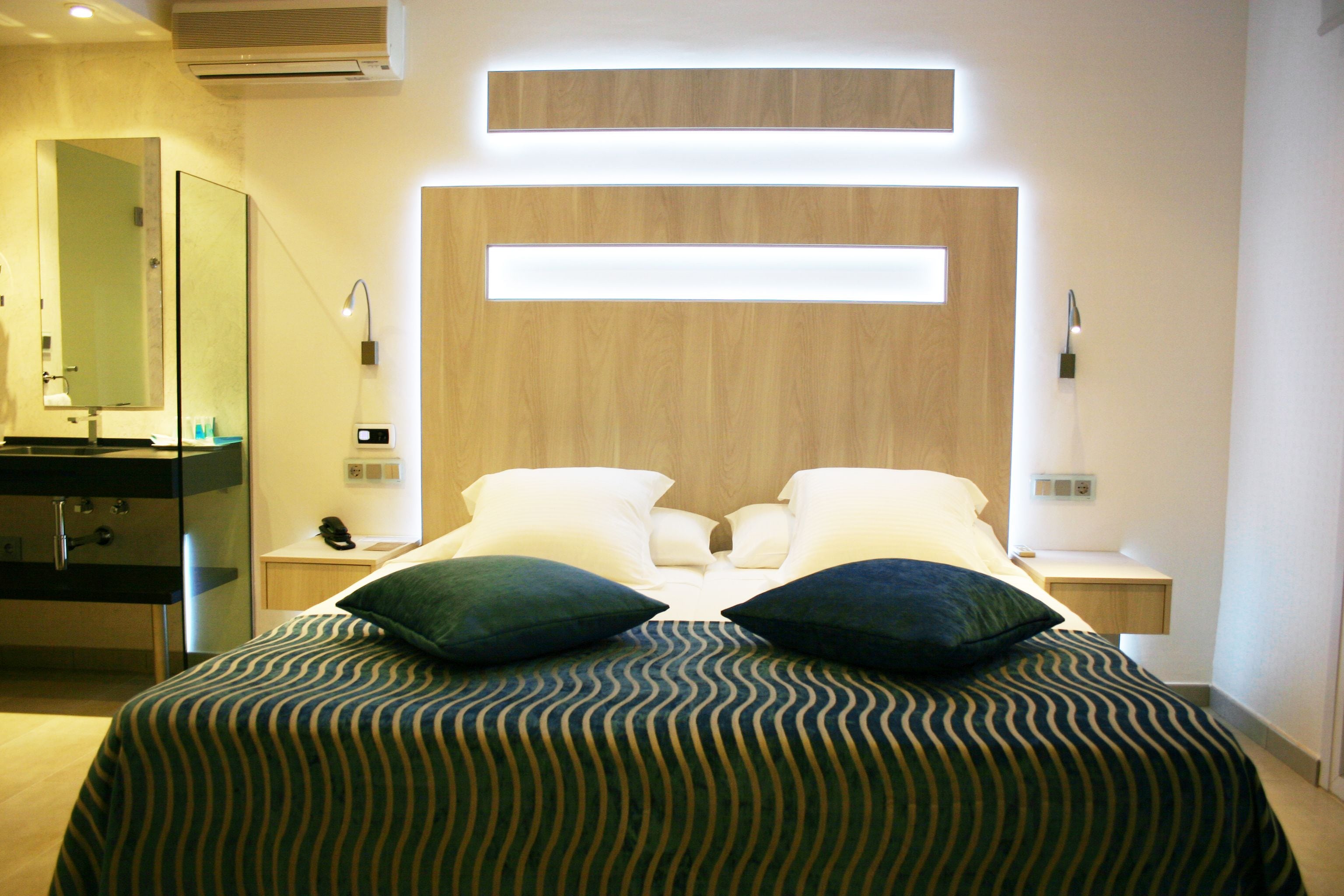 A modern hotel room with a large bed, two bedside tables, a mirror, and a wooden headboard.
