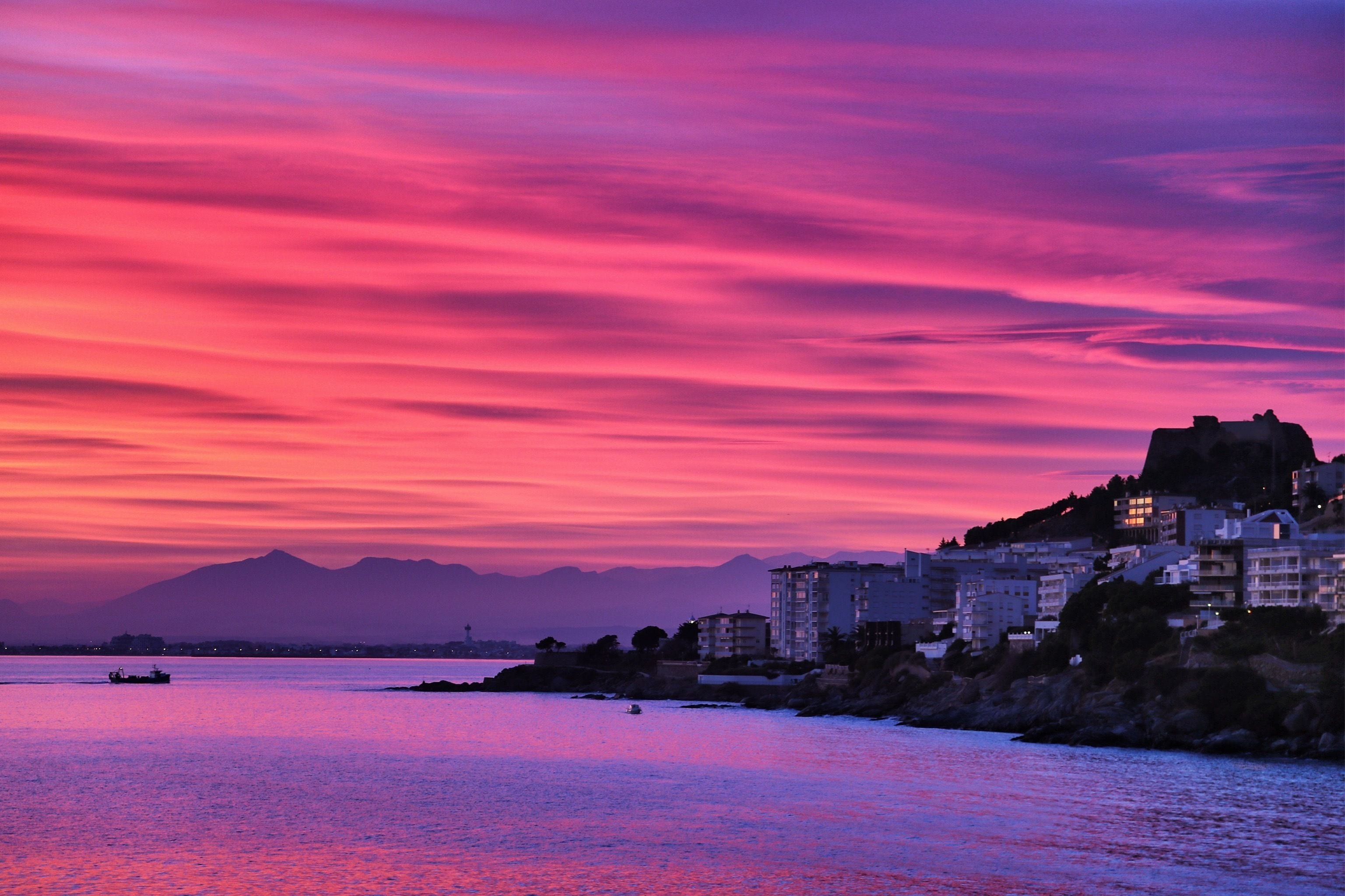 Un paisaje urbano costero al atardecer, con edificios a lo largo de la costa y montañas en el fondo.