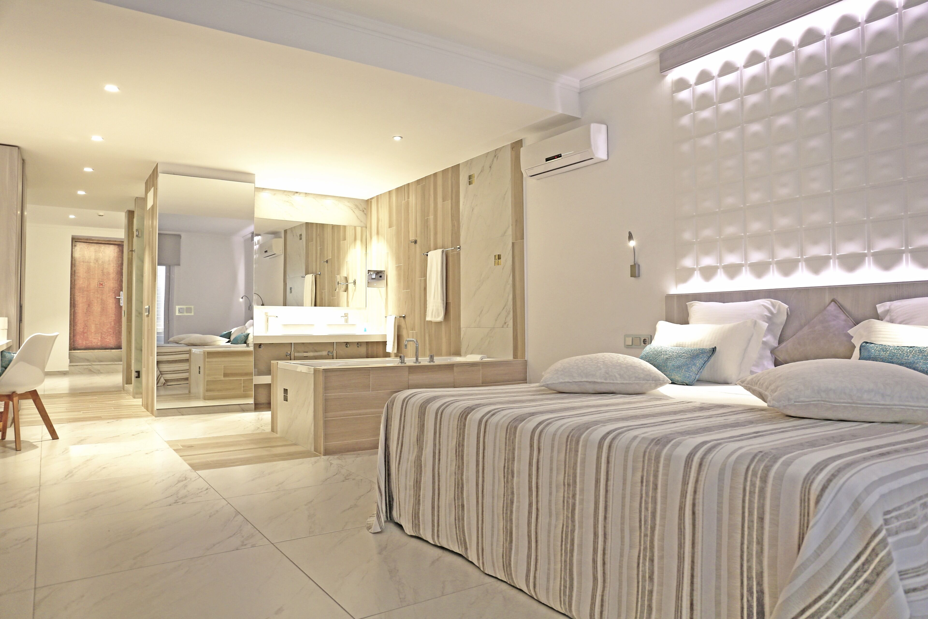 A modern hotel room with a large bed, a separate bathroom with a vanity, and a walk-in closet.
