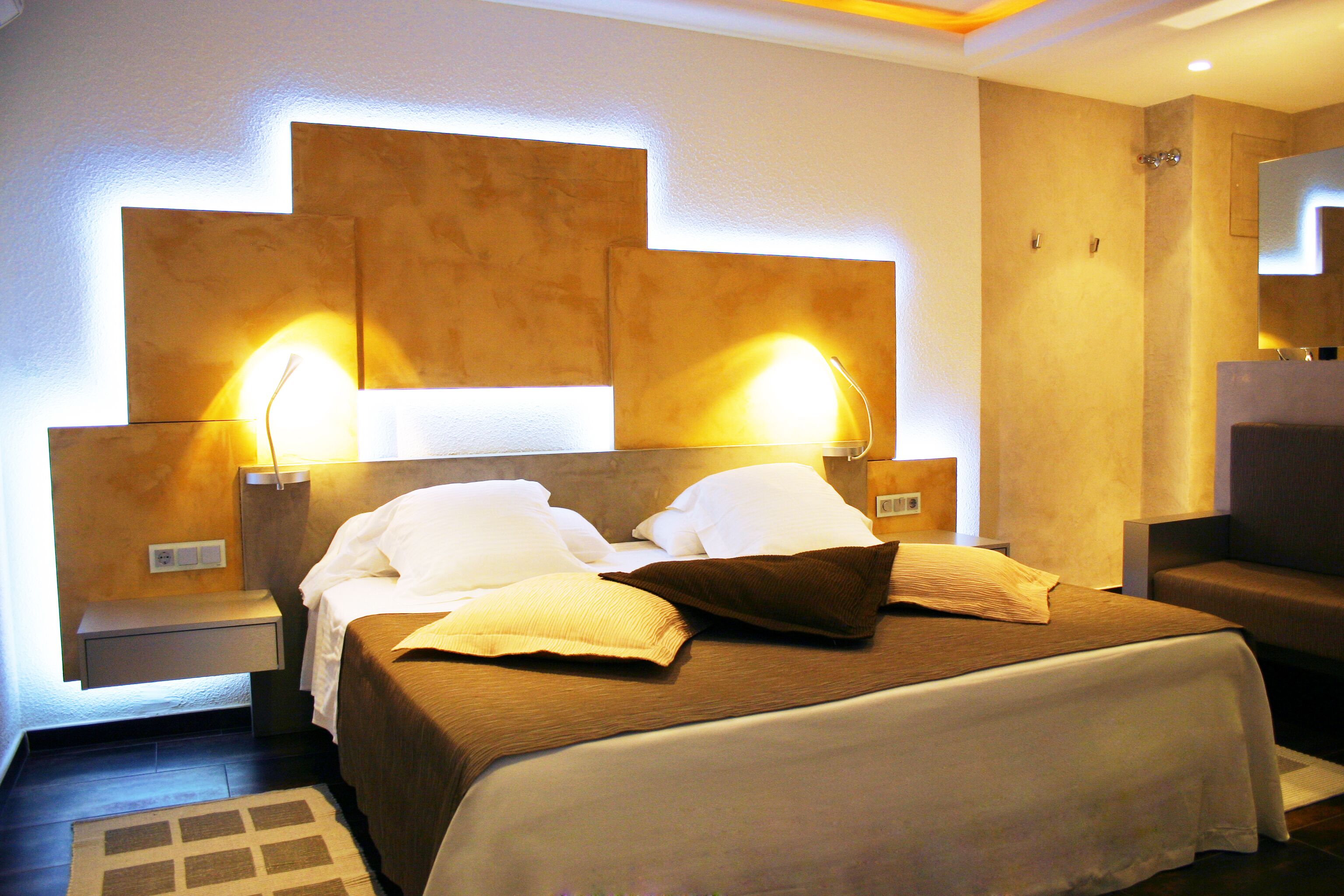 A hotel room with a large bed, two bedside tables, and a headboard with integrated lighting.