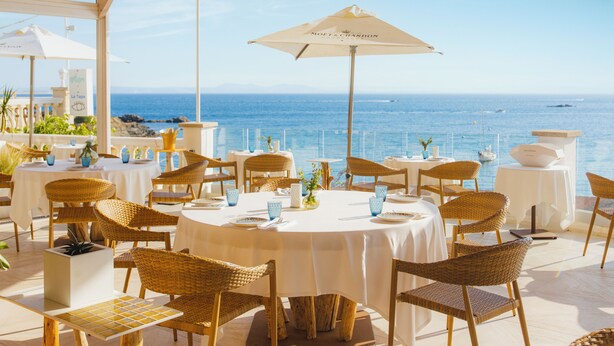 An outdoor dining area with round tables and wicker chairs, overlooking the sea. - Hotel Vistabella (Roses)