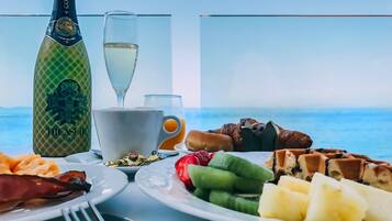 Un desayuno con una botella de 'Treasure Cold' champagne, una copa de vino blanco, y platos con comida variada, incluyendo gofres, fruta y huevos.