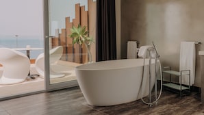 A modern bathroom with a freestanding bathtub, a glass shower enclosure, and a view of the sea through a sliding glass door. - Hotel Vistabella (Roses)