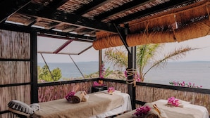 A room with two beds, each with a towel and a small table. The room has a view of the sea and a thatched roof. - Hotel Vistabella (Roses)