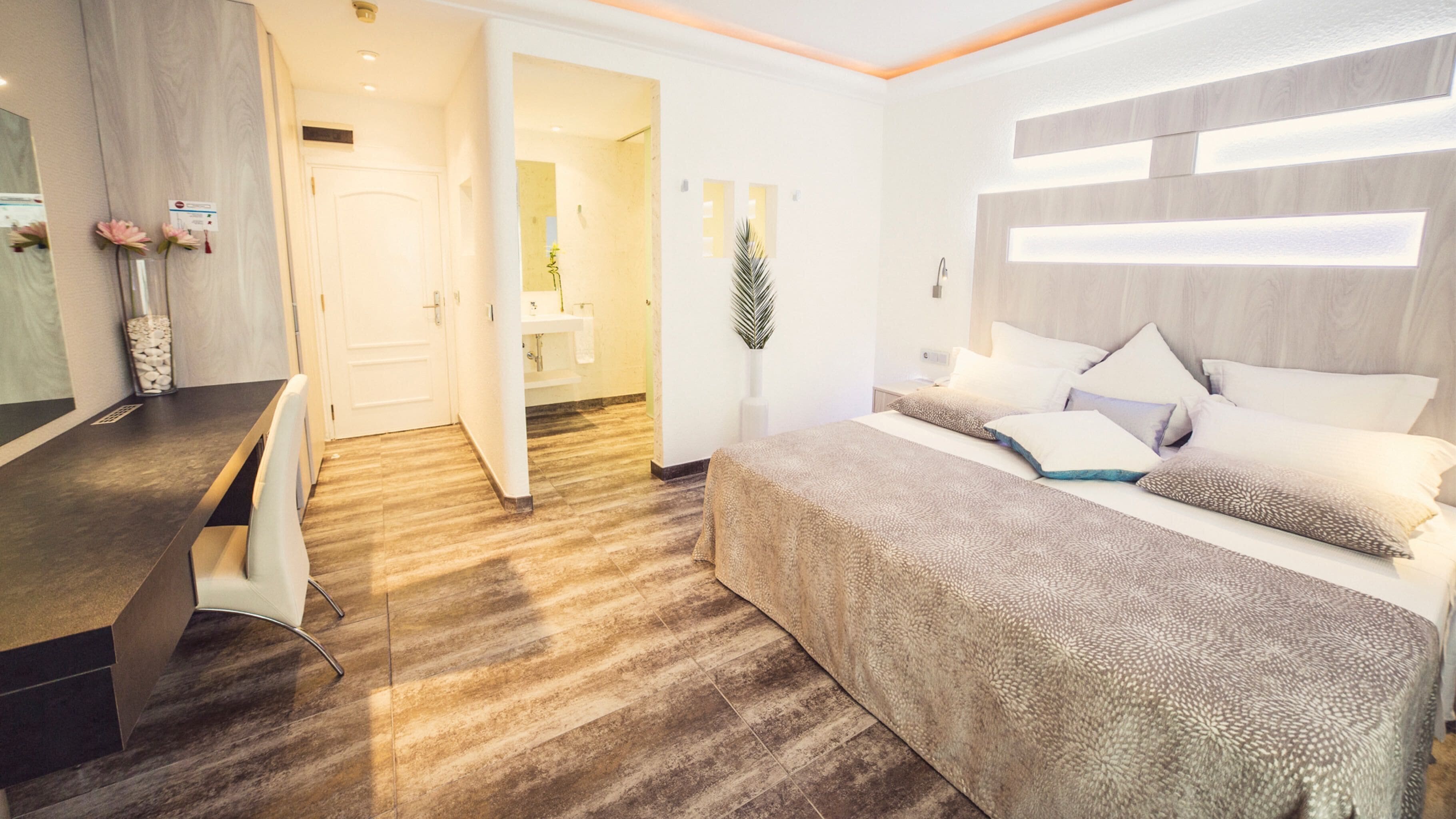 A modern hotel room with a bed, bedside table, and a bathroom visible through an open door.