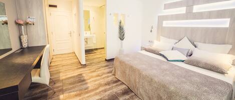 A modern hotel room with a bed, bedside table, and a bathroom visible through an open door.
