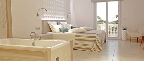A modern bedroom with a large bathtub, a bed with multiple pillows, and a balcony with a view.
