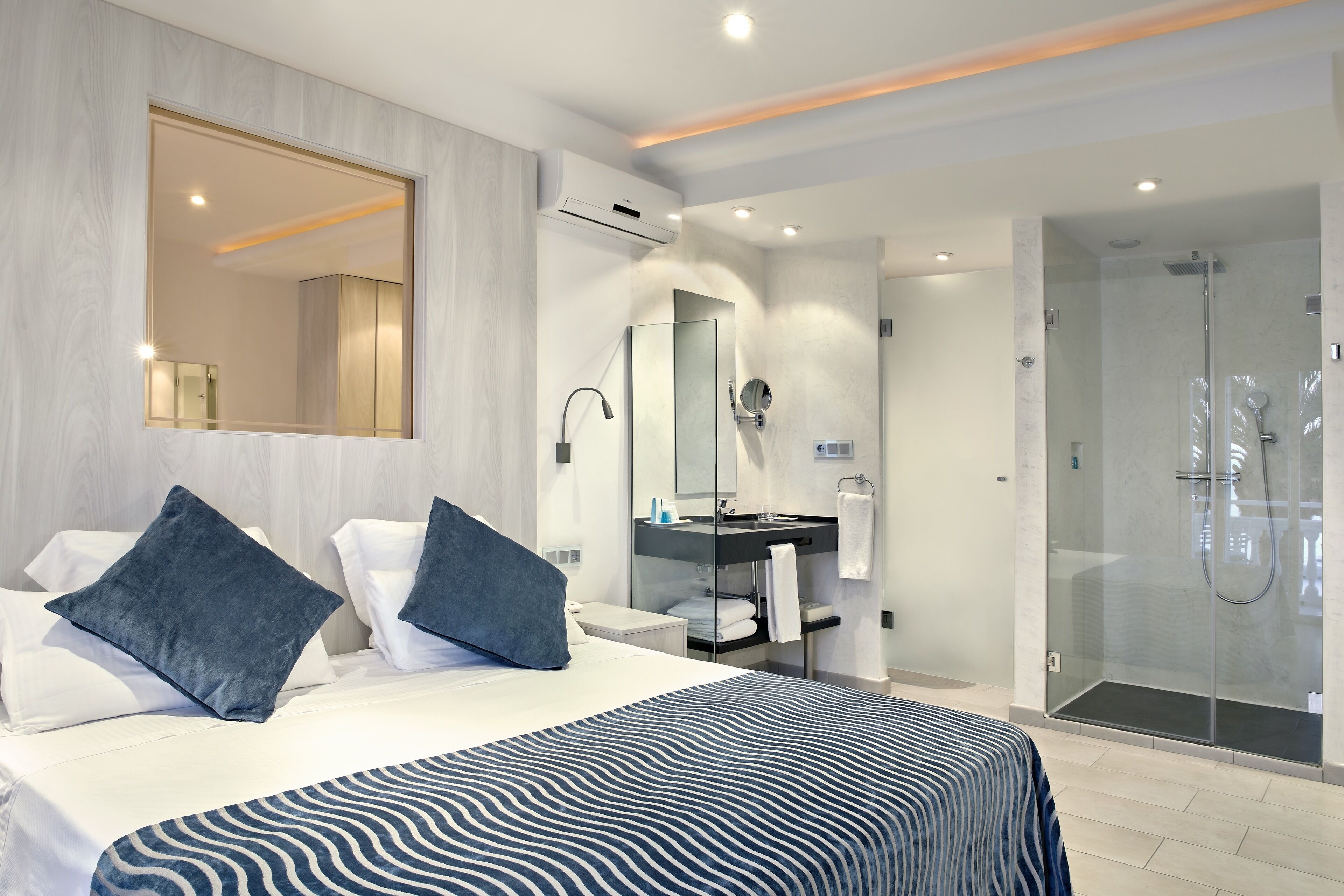 A modern hotel room with a large bed, a bathroom with a glass shower enclosure, and a vanity with a mirror.